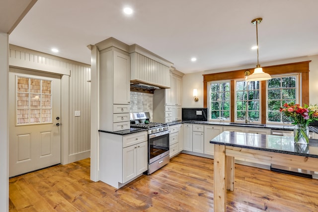 kitchen featuring stainless steel gas range, decorative backsplash, pendant lighting, and light hardwood / wood-style floors