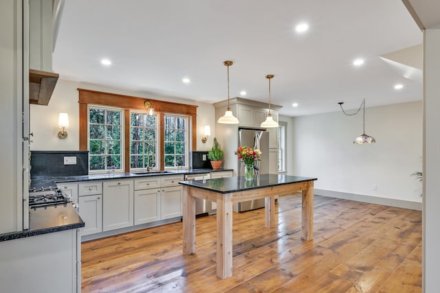 kitchen featuring appliances with stainless steel finishes, decorative backsplash, light wood-type flooring, pendant lighting, and sink