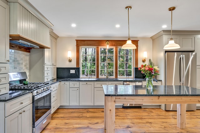 kitchen featuring stainless steel appliances, backsplash, light wood-type flooring, hanging light fixtures, and custom range hood