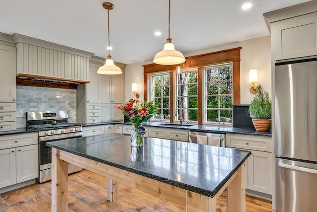 kitchen featuring stainless steel appliances, tasteful backsplash, light wood-type flooring, pendant lighting, and sink