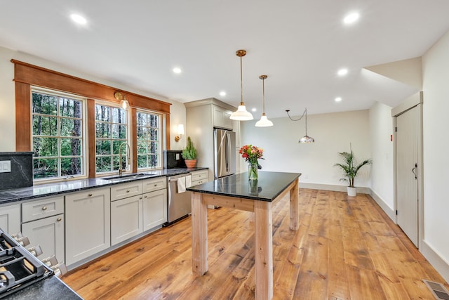 kitchen with decorative light fixtures, tasteful backsplash, sink, light wood-type flooring, and stainless steel appliances