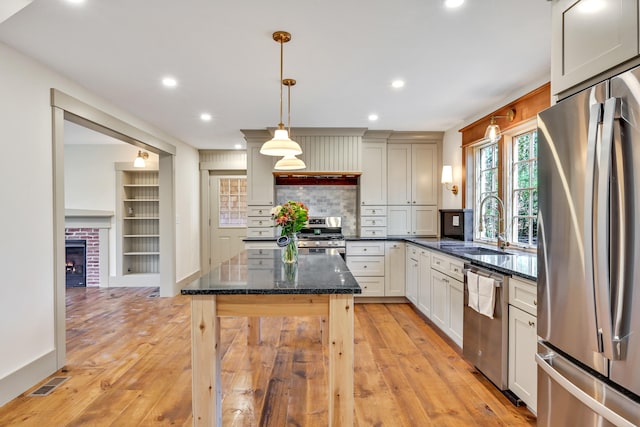 kitchen with a brick fireplace, light hardwood / wood-style floors, sink, hanging light fixtures, and stainless steel appliances