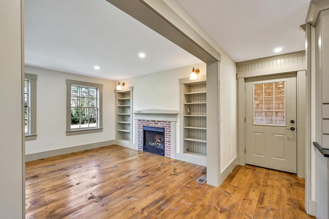 unfurnished living room with a fireplace, built in features, and hardwood / wood-style floors