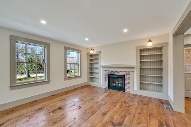 unfurnished living room featuring a brick fireplace, light hardwood / wood-style floors, and built in shelves