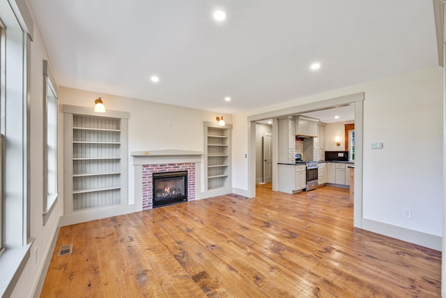 unfurnished living room featuring a brick fireplace, built in shelves, and light hardwood / wood-style flooring