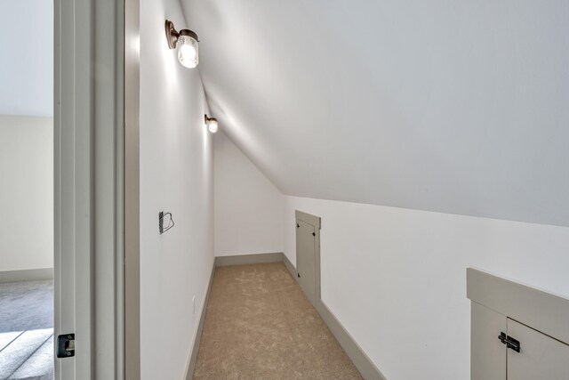 hallway with lofted ceiling and light colored carpet