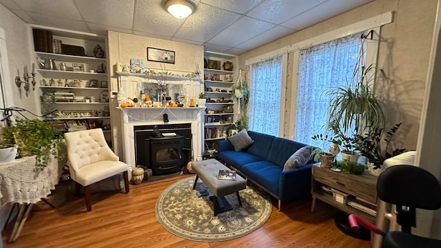 living area featuring a wood stove, hardwood / wood-style floors, a paneled ceiling, and built in features