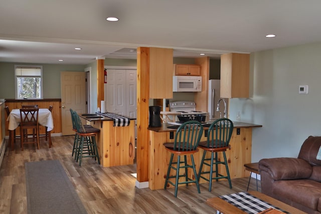 kitchen with a breakfast bar, kitchen peninsula, hardwood / wood-style flooring, and white appliances