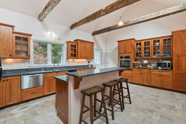 kitchen with appliances with stainless steel finishes, dark stone counters, a kitchen bar, sink, and a center island