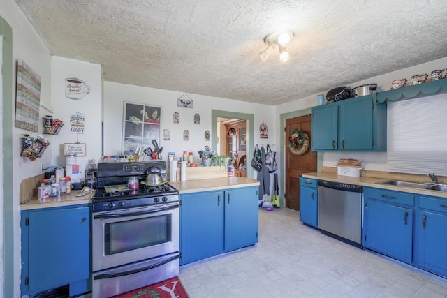 kitchen featuring appliances with stainless steel finishes, blue cabinets, light countertops, light floors, and a sink