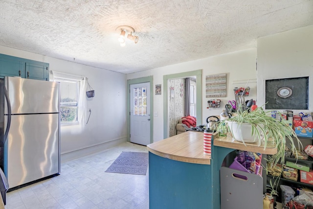 kitchen with blue cabinetry, light floors, light countertops, freestanding refrigerator, and a textured ceiling