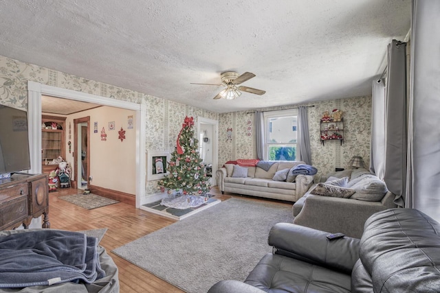 living area featuring a textured ceiling, ceiling fan, baseboards, light wood finished floors, and wallpapered walls