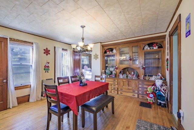 dining space featuring a chandelier, ornamental molding, and light wood-style flooring