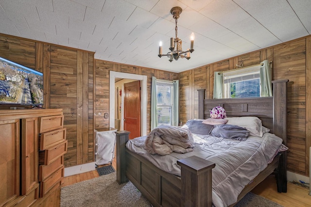 bedroom with light wood-type flooring, wood walls, and a notable chandelier