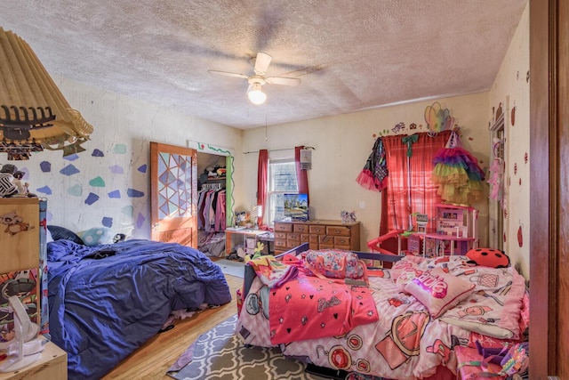 bedroom with ceiling fan, wood finished floors, a walk in closet, a textured ceiling, and a closet