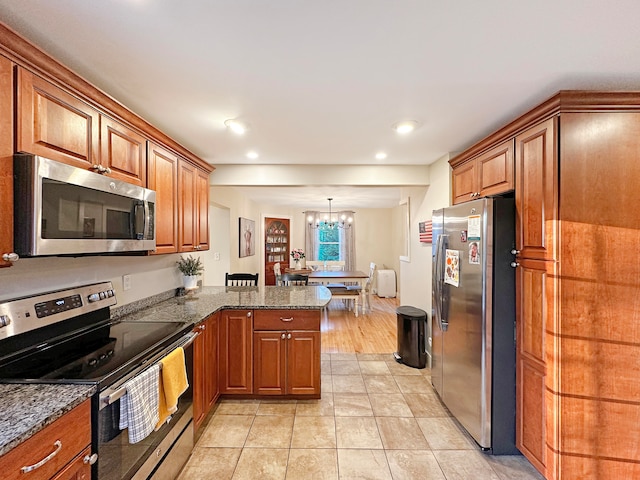 kitchen featuring kitchen peninsula, appliances with stainless steel finishes, a chandelier, light wood-type flooring, and pendant lighting