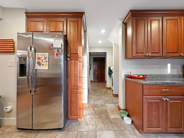 kitchen featuring stainless steel fridge, light tile patterned floors, and dark stone countertops