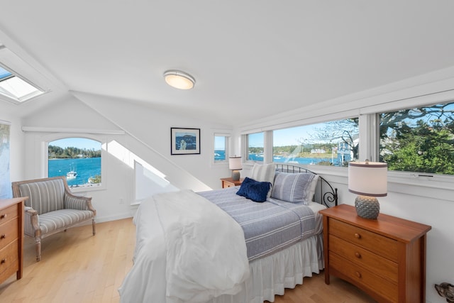 bedroom featuring vaulted ceiling with skylight, multiple windows, a water view, and light wood-type flooring