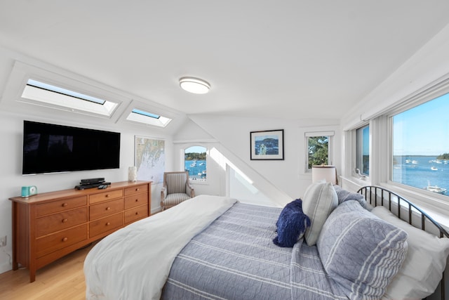 bedroom featuring vaulted ceiling with skylight, a water view, and light wood-type flooring