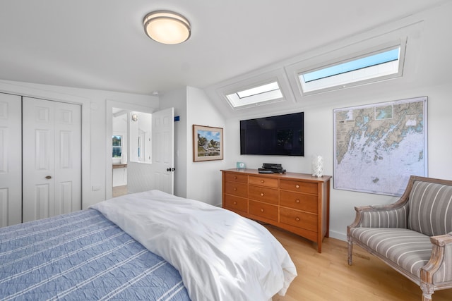 bedroom featuring a closet, light hardwood / wood-style floors, and lofted ceiling with skylight