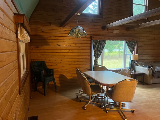 dining room featuring wooden walls, light hardwood / wood-style flooring, and vaulted ceiling with beams