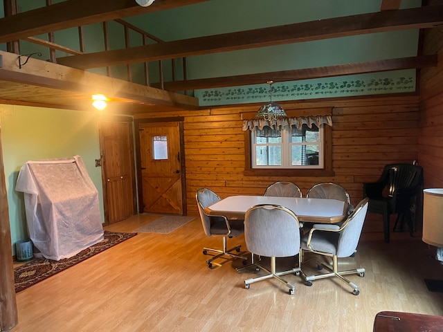 dining room featuring beamed ceiling, wooden walls, and light wood-type flooring