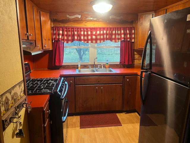 kitchen featuring stainless steel refrigerator, black range with gas stovetop, light hardwood / wood-style floors, sink, and ventilation hood