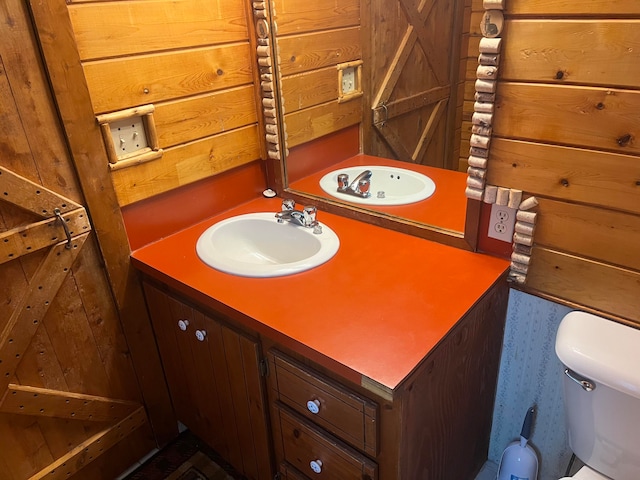 bathroom with vanity, toilet, and wood walls