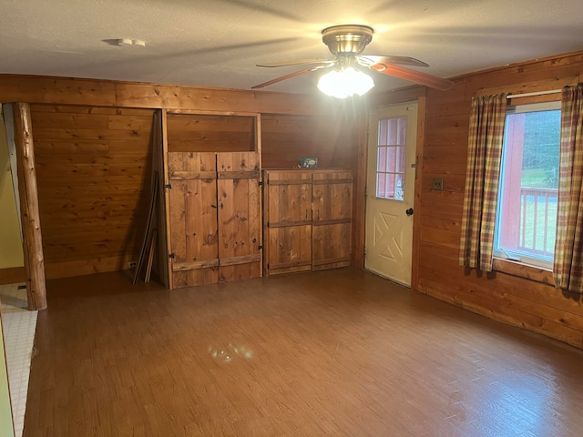 interior space with wooden walls, wood-type flooring, a textured ceiling, and ceiling fan