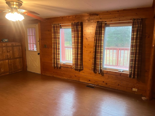 empty room featuring wood walls, wood-type flooring, and plenty of natural light