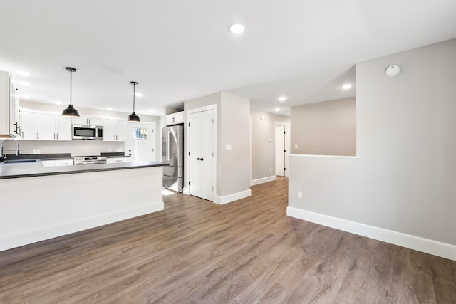 kitchen featuring wood-type flooring, sink, decorative light fixtures, white cabinetry, and appliances with stainless steel finishes