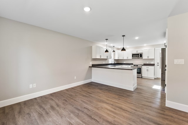 kitchen featuring dark wood-type flooring, kitchen peninsula, stainless steel appliances, pendant lighting, and white cabinets