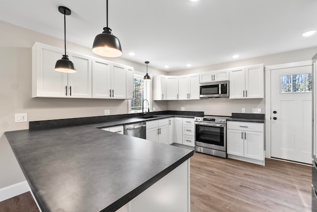 kitchen with white cabinets, appliances with stainless steel finishes, light wood-type flooring, sink, and decorative light fixtures