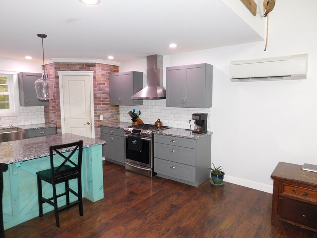 kitchen featuring stainless steel range with gas cooktop, dark wood finished floors, gray cabinetry, a wall mounted AC, and wall chimney range hood