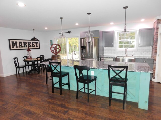 kitchen with a spacious island, a sink, backsplash, dark wood-style floors, and stainless steel fridge