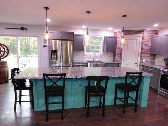 kitchen featuring a sink, appliances with stainless steel finishes, decorative backsplash, light stone countertops, and dark wood finished floors