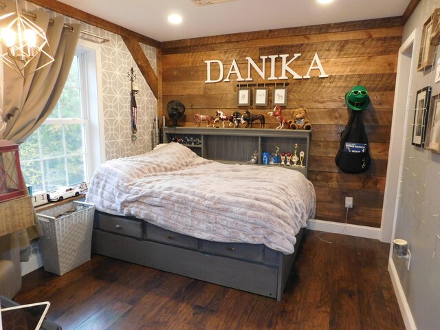 bedroom with baseboards, an inviting chandelier, wood finished floors, and wooden walls