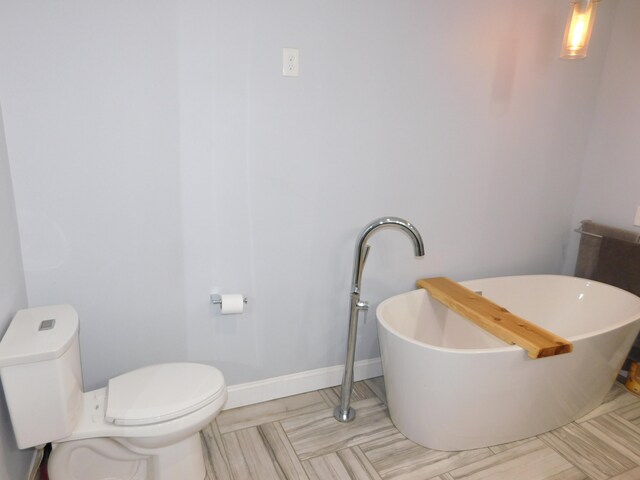 full bathroom with a freestanding bath, toilet, and baseboards