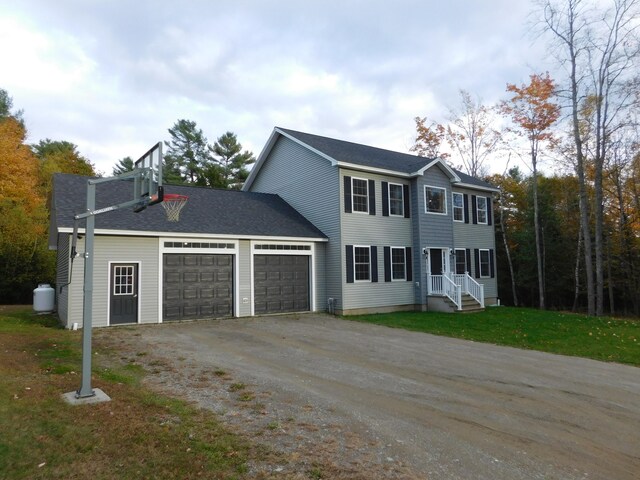 colonial home featuring a garage, driveway, a shingled roof, and a front yard