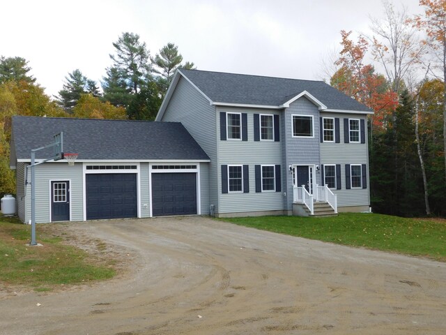 colonial-style house with an attached garage, driveway, a front lawn, and roof with shingles