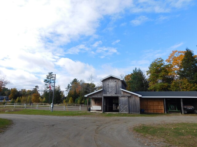 view of barn with dirt driveway and fence