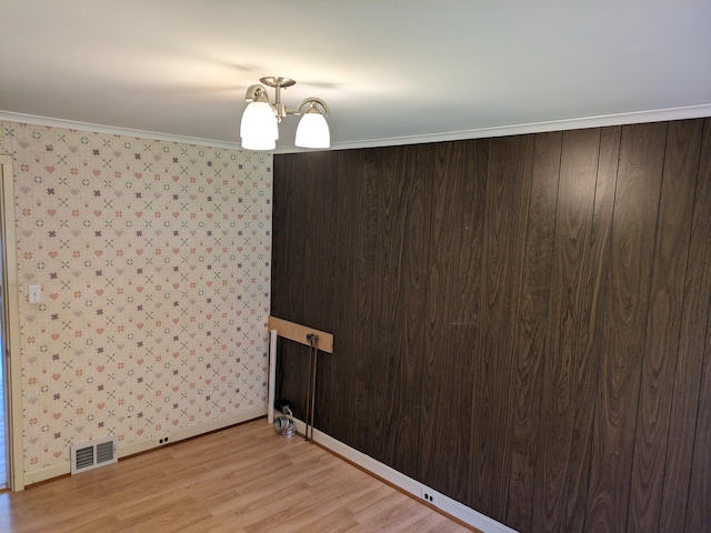 empty room featuring crown molding, a notable chandelier, and light wood-type flooring