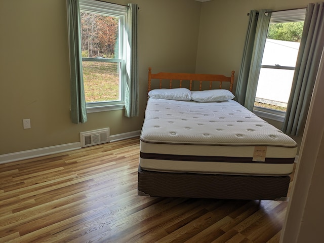 bedroom featuring baseboards, visible vents, multiple windows, and wood finished floors