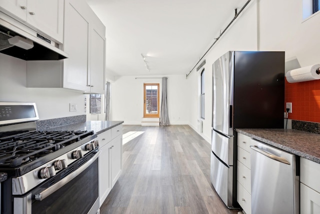 kitchen with white cabinets, decorative backsplash, dark stone countertops, light wood-type flooring, and stainless steel appliances