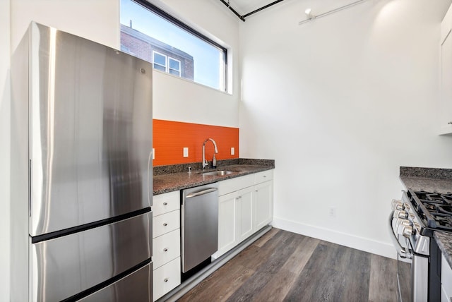 kitchen with sink, dark hardwood / wood-style flooring, dark stone countertops, white cabinets, and appliances with stainless steel finishes