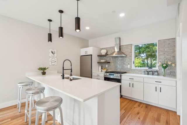 kitchen featuring wall chimney range hood, white cabinets, stainless steel appliances, pendant lighting, and sink