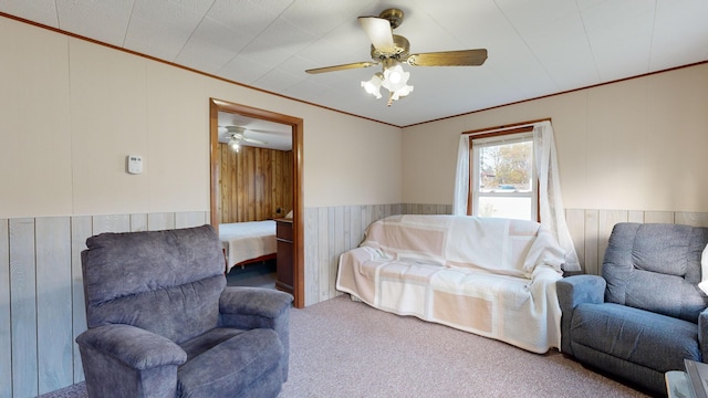 living room featuring ornamental molding, wooden walls, carpet, and ceiling fan