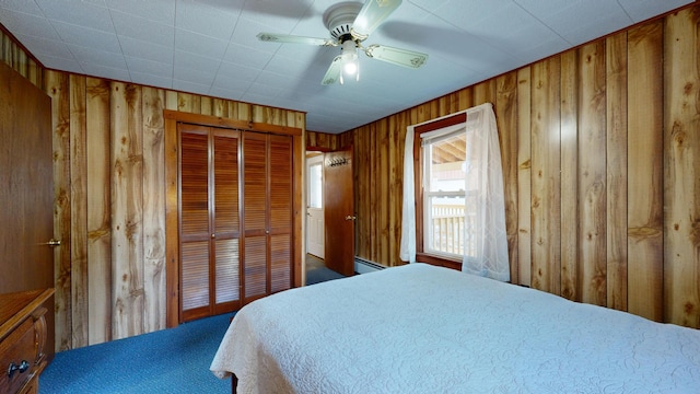 bedroom with a closet, ceiling fan, a baseboard radiator, and wooden walls