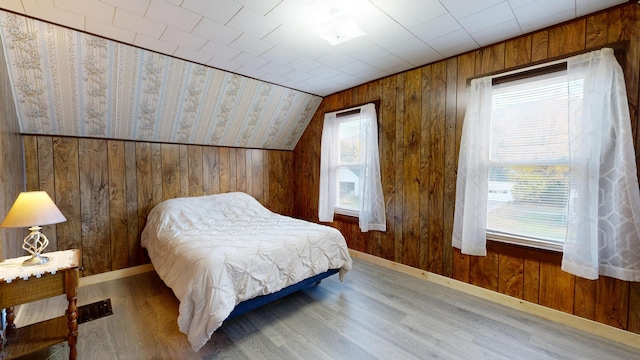 bedroom featuring wooden walls, wood-type flooring, and vaulted ceiling