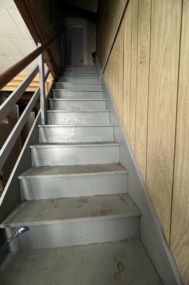 staircase with concrete floors and wood walls